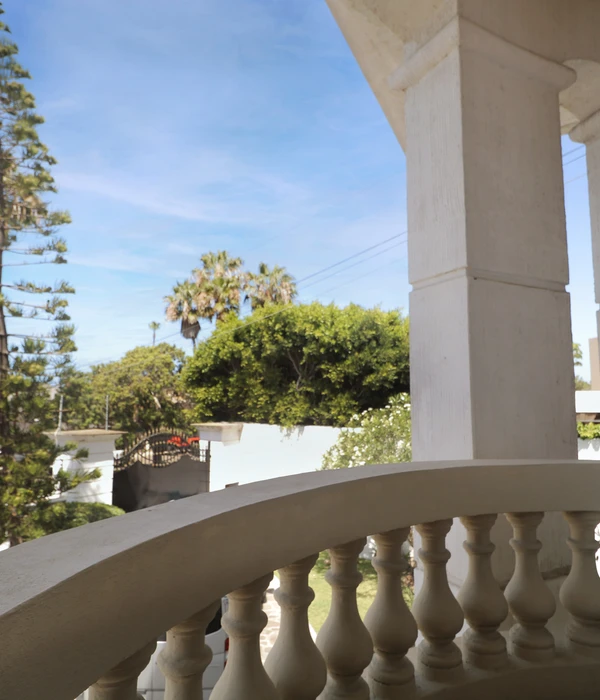 View from a balcony with a white balustrade overlooking a garden with palm trees and a wall, under a blue sky.