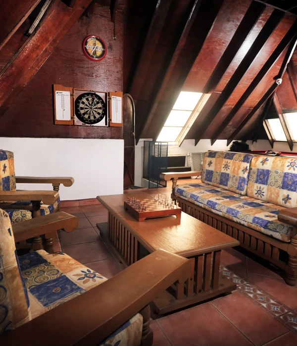 A cozy game room in an attic with a dartboard, a chess set on a coffee table, and patterned sofas under sloped wooden ceilings.
