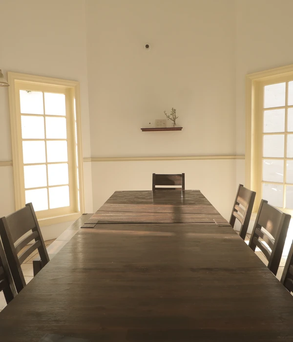 Long wooden table with chairs in a bright, white room with large windows providing natural sunlight.