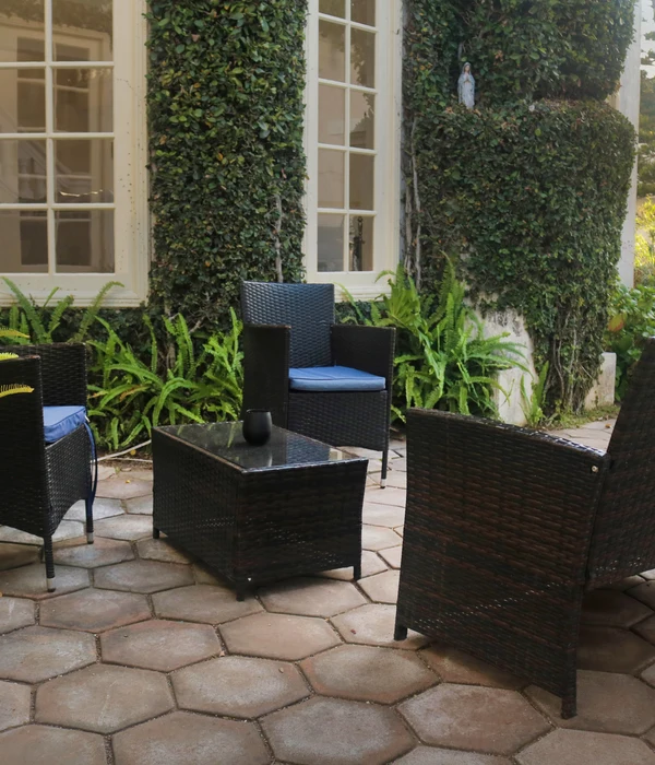 Outdoor patio with dark wicker chairs and a matching coffee table on hexagonal pavers, set against a lush, ivy-covered wall.