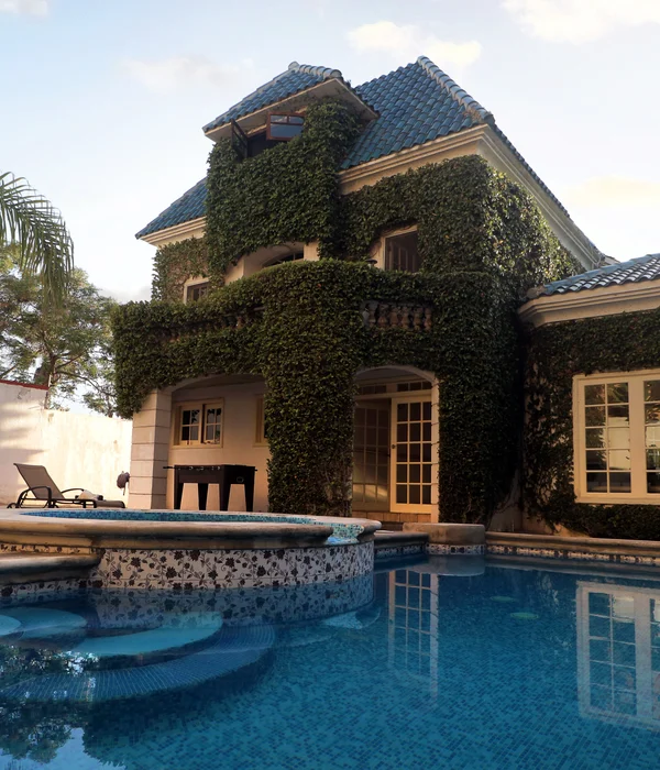 View of an outdoor swimming pool and tiled jacuzzi in front of a multi-story building covered in lush green ivy.